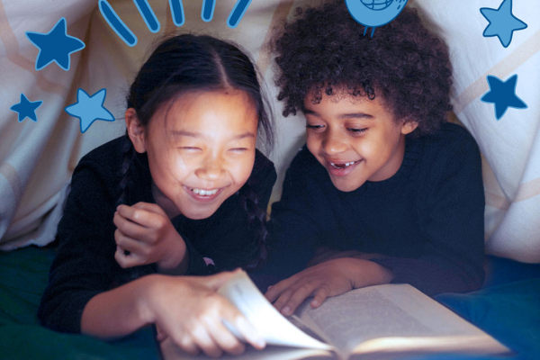 Two kids smiling and reading a book.