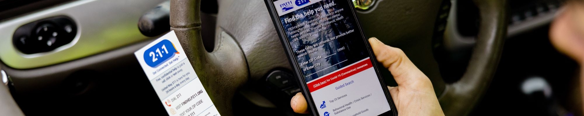 A person holds a smartphone displaying the FindHelp211.org website.