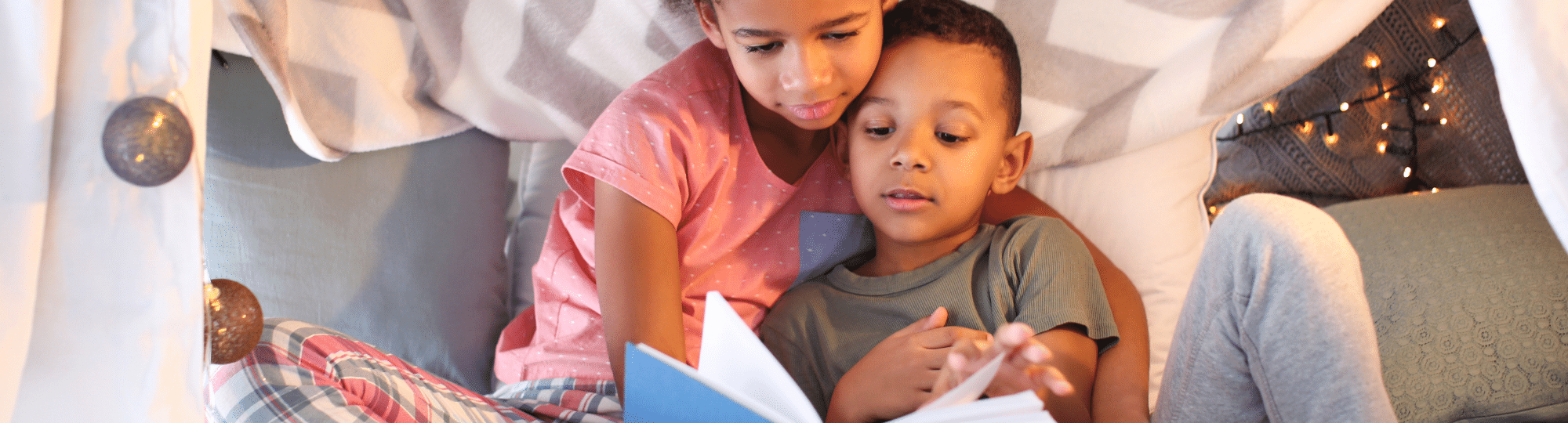 two children reading a book in a pillow fort