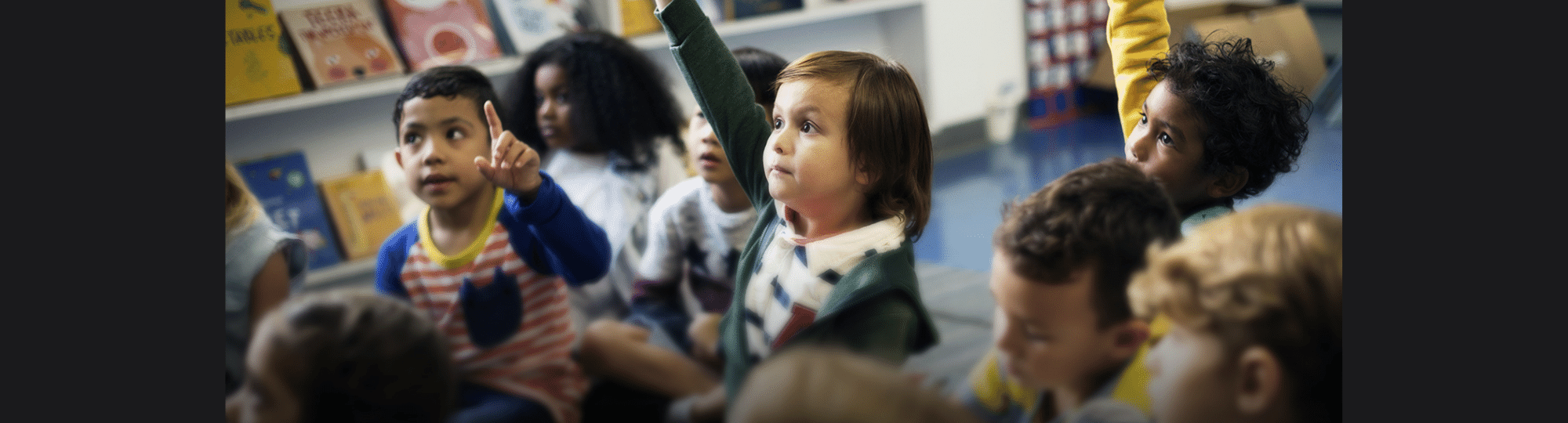 Kindergartener raising their hand in a classroom.
