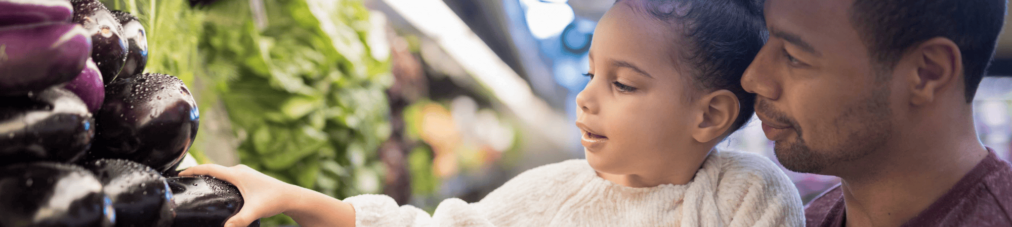 dad helping girl pick vegetables at store