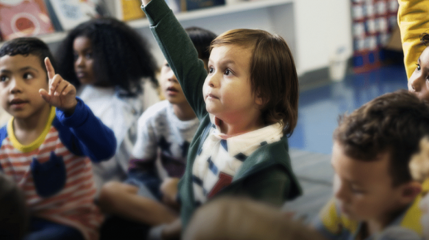 Kindergartener raising their hand in a classroom.